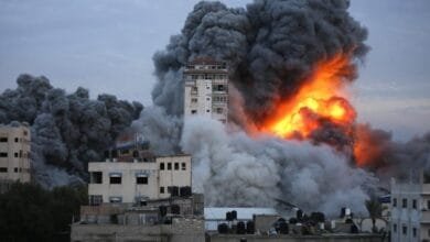 A building engulfed in flames and thick black smoke after an airstrike in Gaza. Surrounding buildings are also damaged.