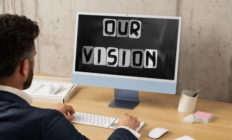 A person sits at a desk, working on a computer displaying the words 'Our Vision' in a chalkboard style.