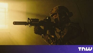Silhouetted soldier aiming a rifle with a laser sight in a dimly lit room.