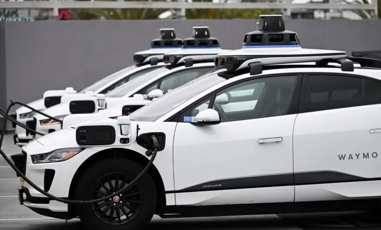 Several white Waymo self-driving Jaguar I-PACE electric vehicles are parked and charging at an EVgo station.