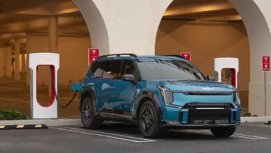 A teal Kia EV6 SUV charges at a Tesla Supercharger station in a modern parking garage.