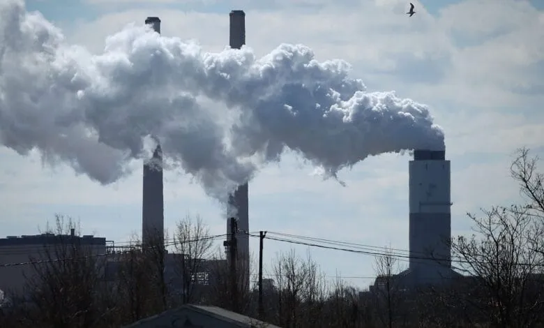 Thick plumes of smoke billow from tall industrial smokestacks against a partly cloudy sky.