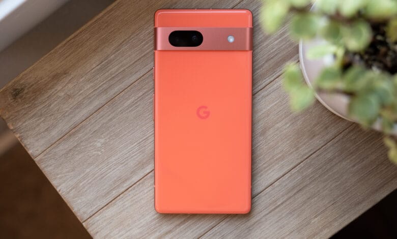 Coral Google Pixel phone rests on a light wood surface, next to a small potted plant.