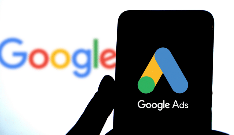 Close-up of a phone displaying the Google Ads logo against a blurred Google background.