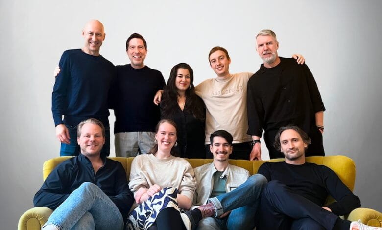 Ten smiling colleagues, five men and five women, pose for a team photo on a yellow couch. Casual attire, friendly atmosphere.