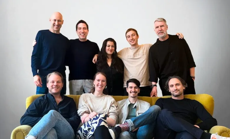 A diverse team of ten smiling colleagues, five men and five women, pose together on a bright yellow couch.