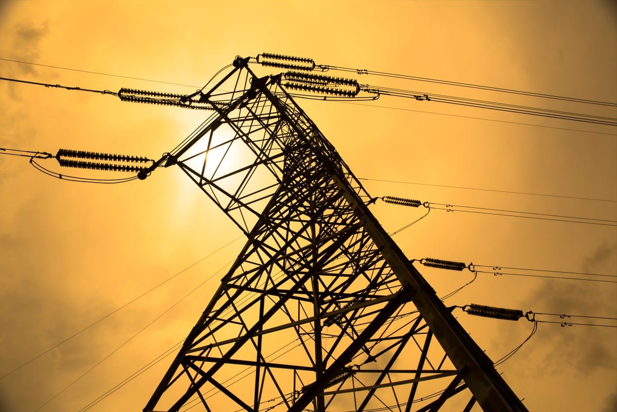 Silhouette of a tall electricity pylon against a vibrant orange sunset sky.