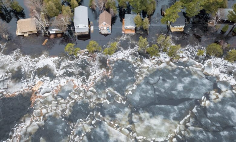 Aerial view of flooded cottages on Grand Lake, New Brunswick, surrounded by broken ice floes. Water levels are high, threatening the properties.