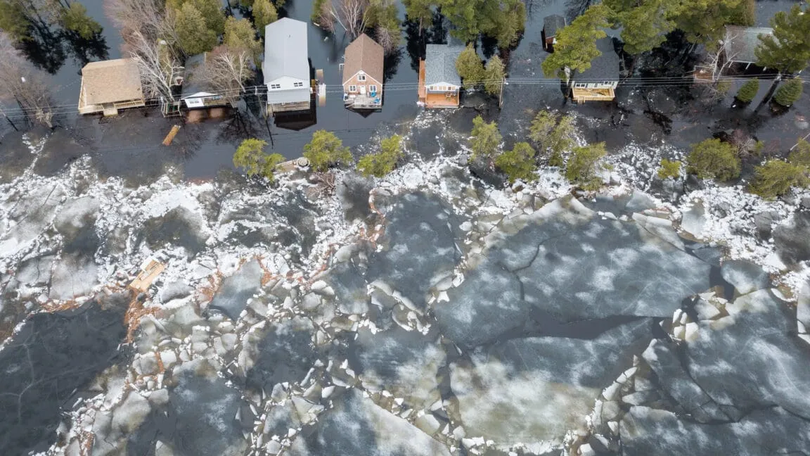 Aerial view of flooded cottages on Grand Lake, New Brunswick, surrounded by broken ice floes. Water levels are high, threatening the properties.