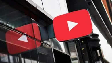 A bright red YouTube logo with a white play button is mounted on a modern building's glass exterior. Its reflection is visible.