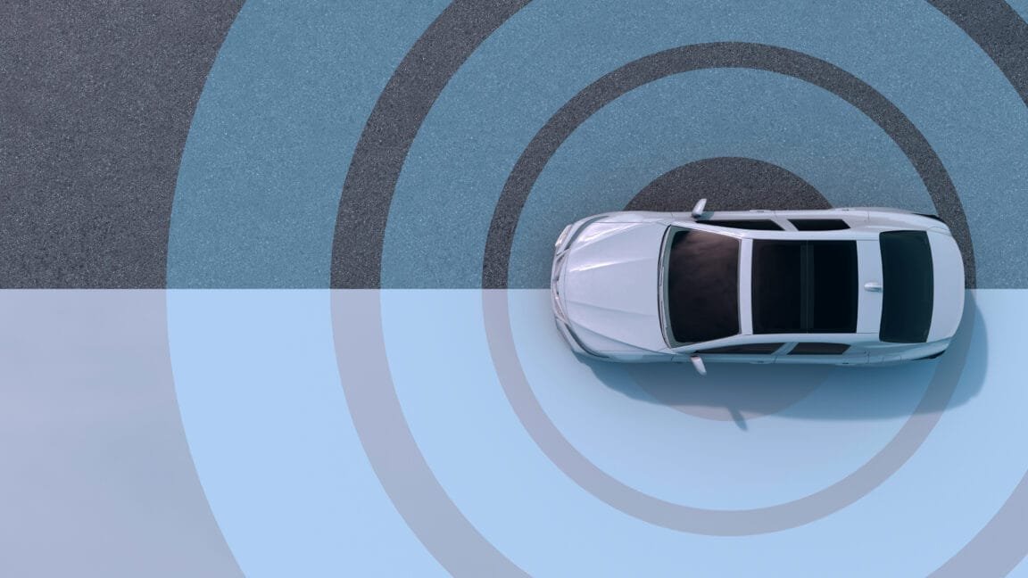 Overhead view of a white self-driving car navigating a road depicted with concentric circles, suggesting its sensor range.