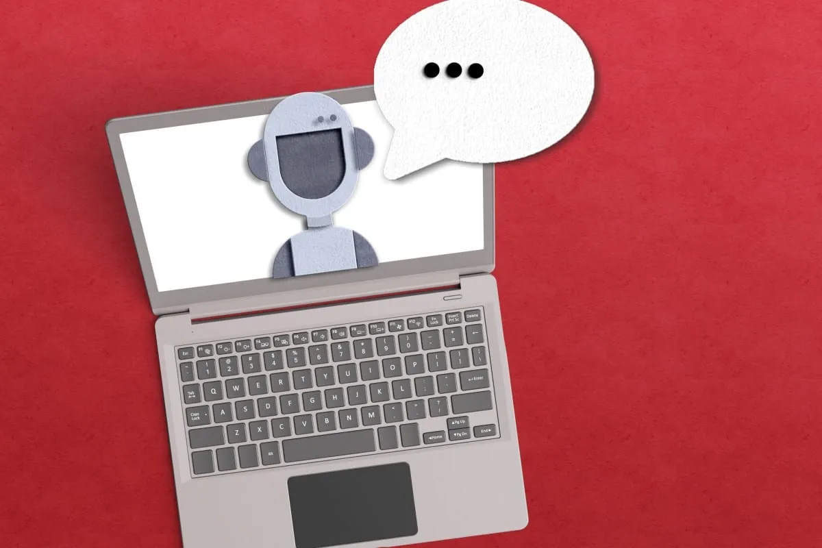 Laptop screen displays a paper robot with a speech bubble, suggesting AI customer service or chatbot interaction.