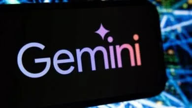 Close-up of a smartphone displaying the Gemini cryptocurrency exchange logo. Blurred network cables in the background.