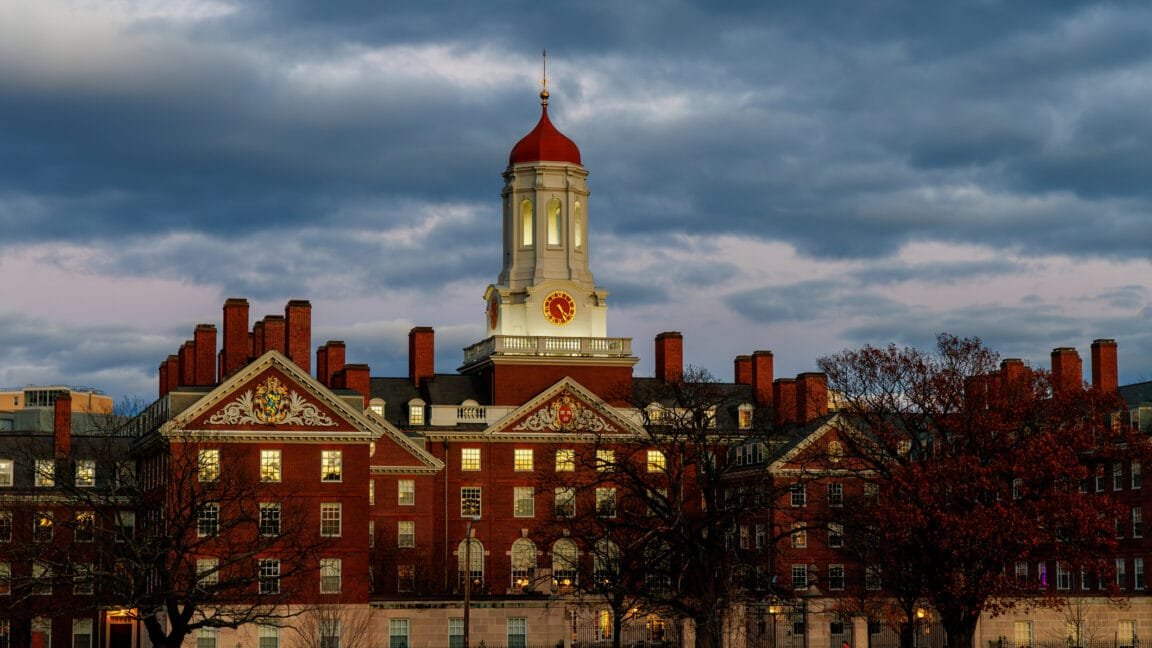 Harvard University's Dunster House at twilight, showcasing its red brick facade, clock tower, and autumnal trees.