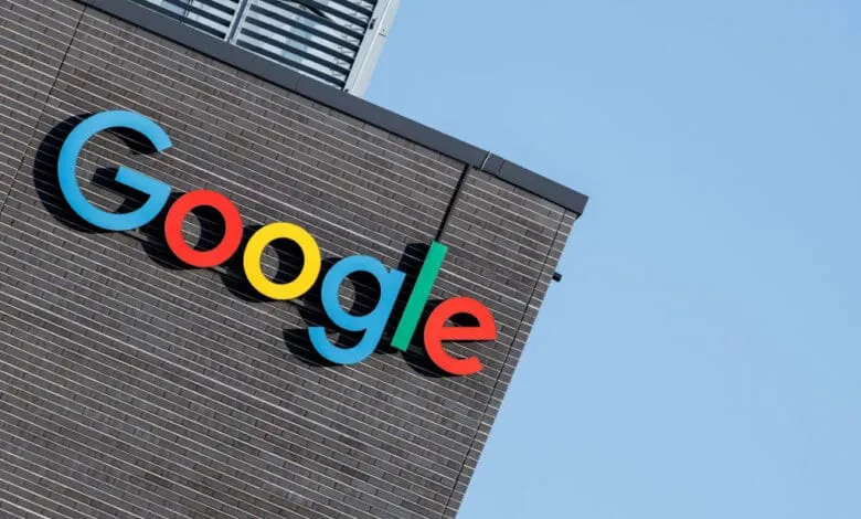 The colorful Google logo is mounted on a dark gray brick building against a clear blue sky.