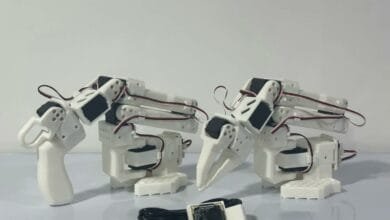 Two white robotic arms with claw-like grippers and a small camera module.