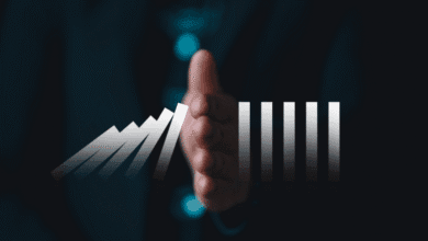 Hand stopping falling dominoes; some dominoes represent growth, others stability. Dark background.