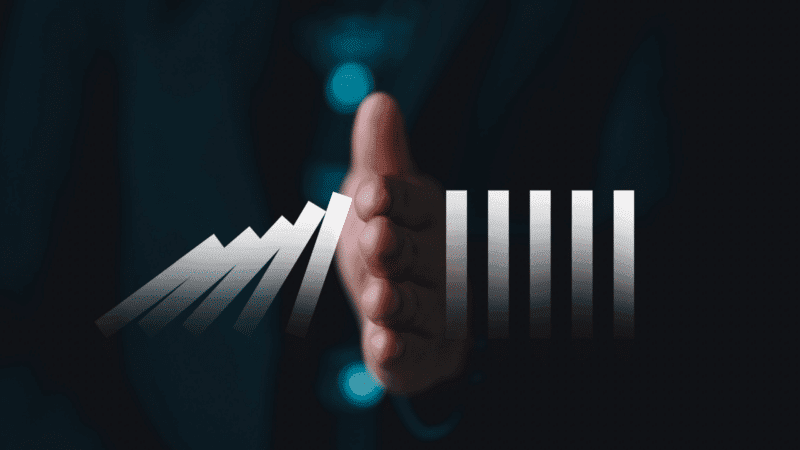 Hand stopping falling dominoes; some dominoes represent growth, others stability. Dark background.