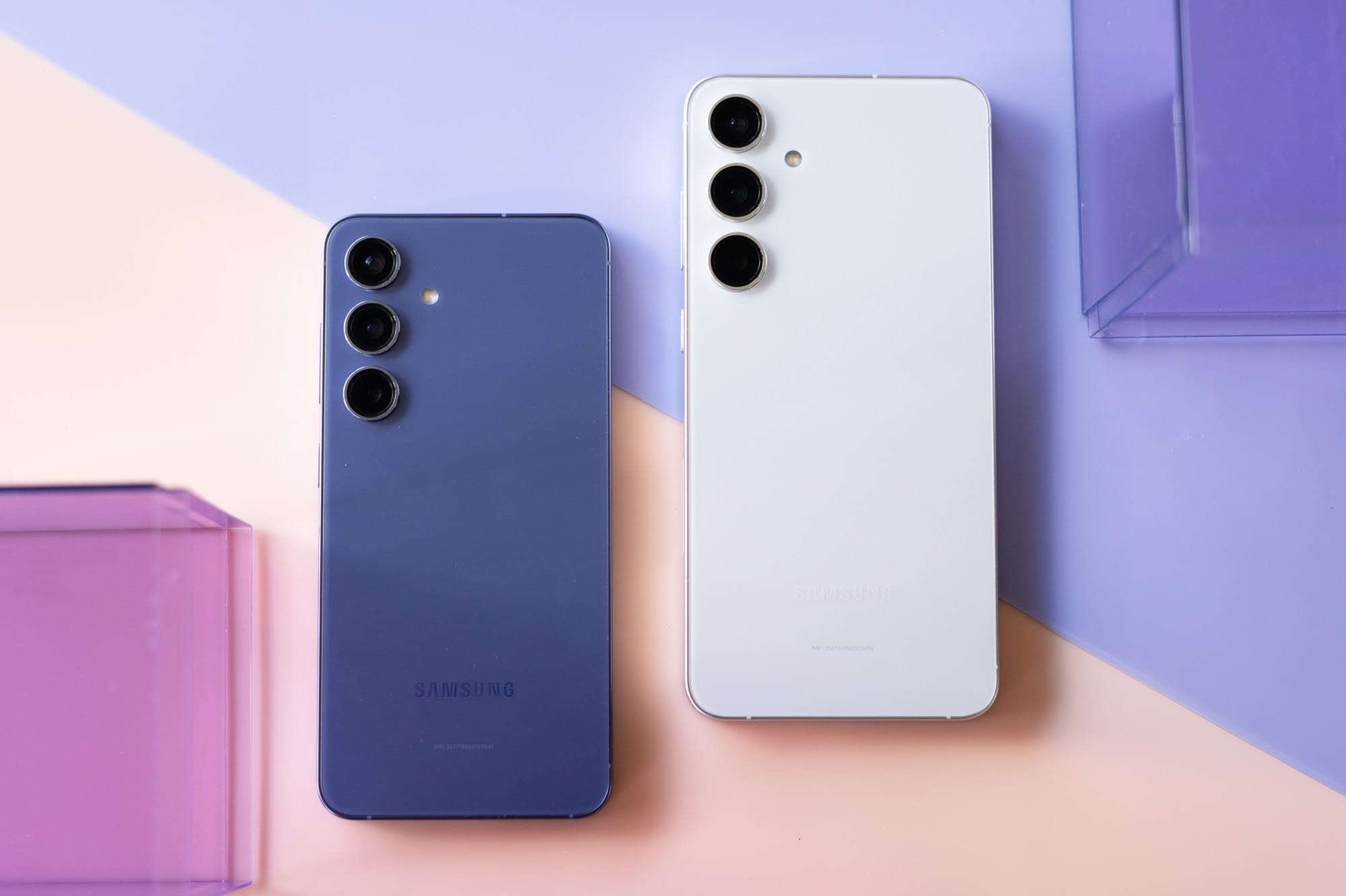 Two Samsung smartphones, one purple and one white, lie on a pastel background. Their triple-lens cameras are visible.