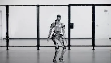 A silver humanoid robot stands behind a clear safety barrier in a modern, minimalist room.