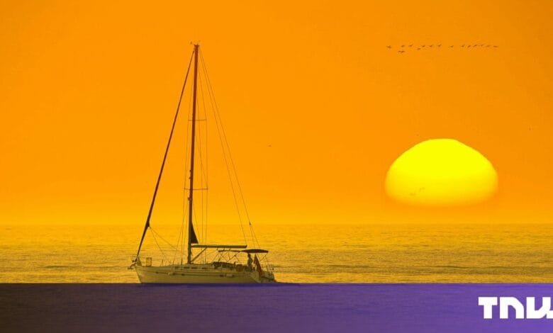 Silhouette of a sailboat on calm ocean water at sunset, large yellow sun in the sky, birds flying.