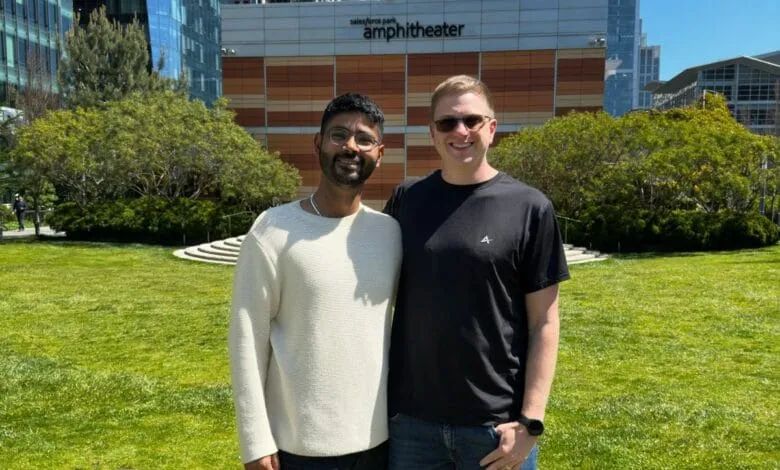 Two men stand smiling outside the Salesforce Park Amphitheater on a sunny day.