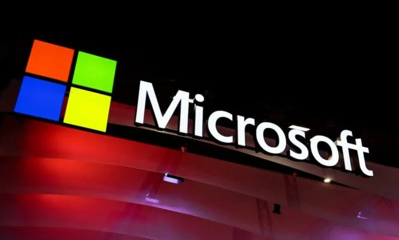 Illuminated Microsoft logo with its four-color square and white lettering against a dark red background.