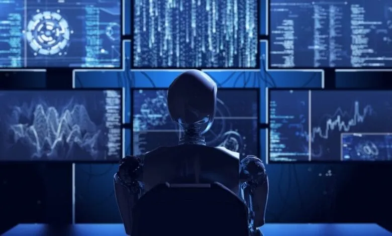 A robot sits before multiple computer screens displaying complex data streams and graphs in shades of blue.