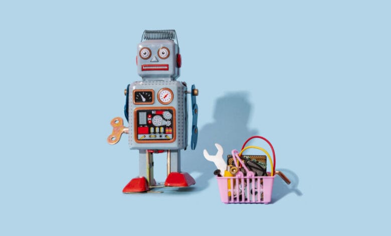 A vintage tin robot stands next to a small pink shopping basket filled with mechanical parts against a light blue background.
