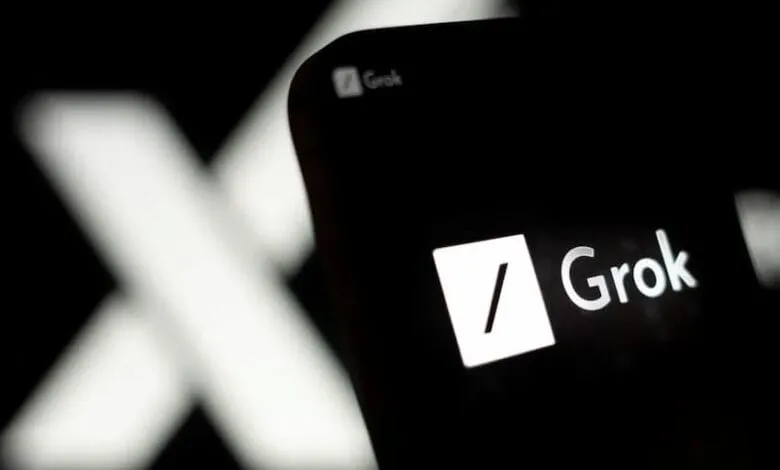 Close-up of a smartphone displaying the Grok AI app logo. A blurred 'X' is visible in the background.