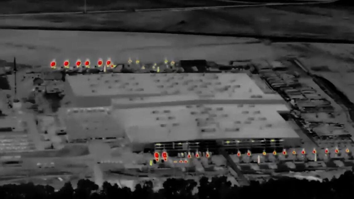 Aerial thermal image of an industrial building at night. Red hotspots show high heat emission from machinery.