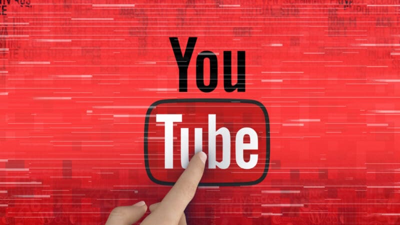Finger points to YouTube logo on a red background with white streaks, suggesting fast-paced digital content.