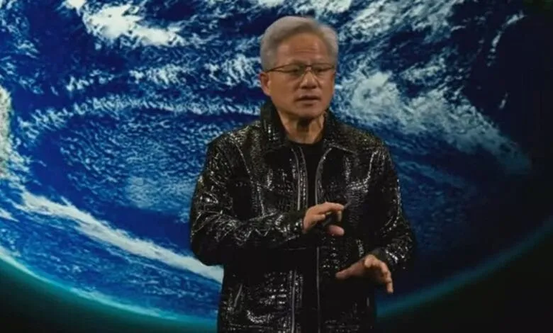 A man in a black leather jacket gestures while standing in front of a backdrop showing Earth from space.