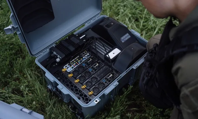 A person inspects the open case of a complex piece of technology in a grassy field.