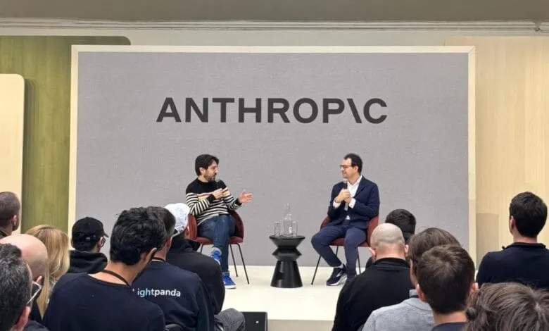 Two men, Dario Amodei and another, sit on stage at an Anthropic event, speaking to a large audience.