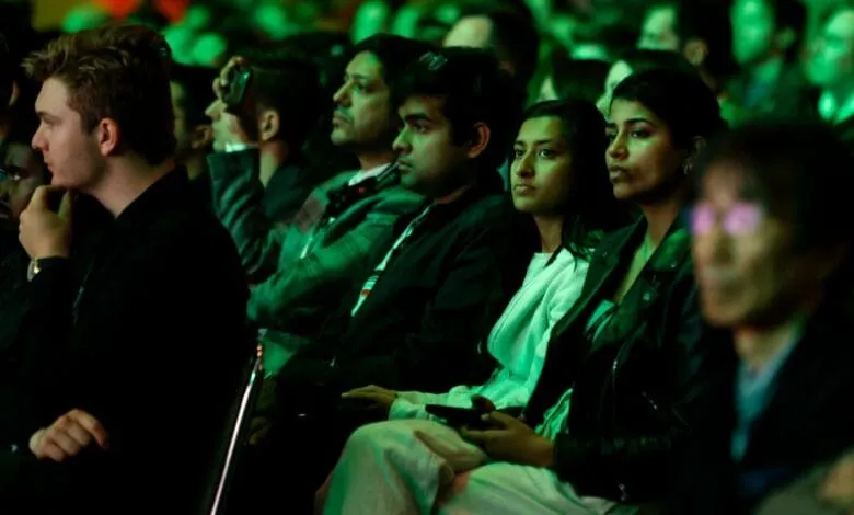 Audience members attentively listen during a presentation, bathed in green light.