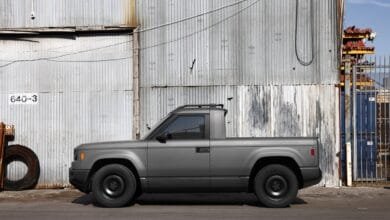 Side profile of a dark gray electric pickup truck parked against a corrugated metal wall.