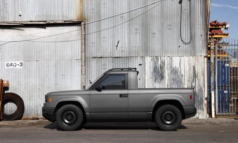 Side profile of a dark gray electric pickup truck parked against a corrugated metal wall.