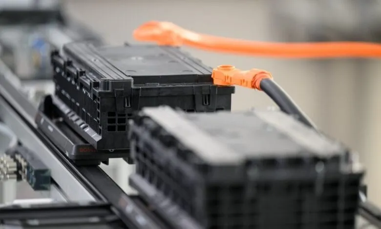 Close-up of black Bosch electric vehicle batteries on a conveyor belt, connected by an orange cable.