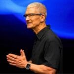 Tim Cook, Apple CEO, speaks at a presentation against a vibrant blue backdrop.