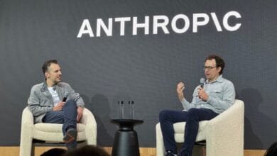 Two men in casual clothes converse on stage, seated in fluffy white chairs. 'ANTHROPIC' is displayed on a screen behind them.
