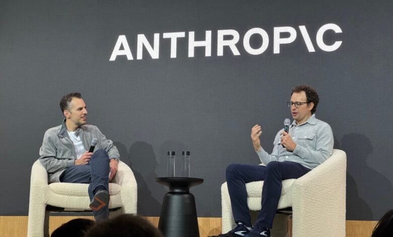 Two men in casual clothes converse on stage, seated in fluffy white chairs. 'ANTHROPIC' is displayed on a screen behind them.