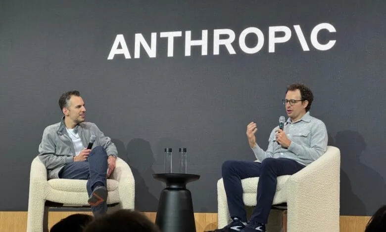 Two men in casual clothes converse on stage, seated in fluffy white chairs. 'ANTHROPIC' is displayed on a screen behind them.