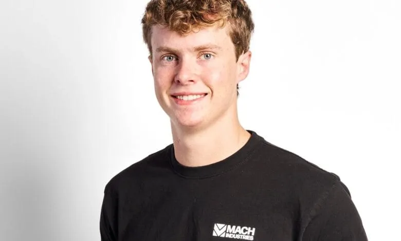 Smiling young man, Ethan Thornton, with curly light brown hair wearing a black Mach Industries t-shirt against a white background.