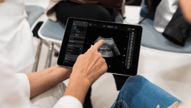 Close-up of a doctor's hands using a tablet to view an ultrasound image, showing medical details and patient information.