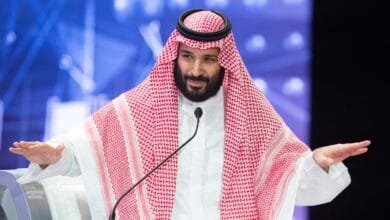 Crown Prince Mohammed bin Salman speaks at a conference, wearing traditional Saudi Arabian attire.