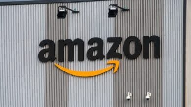 Large Amazon logo on a corrugated metal building, with security lights and cameras.