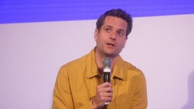 Klarna CEO in mustard yellow shirt speaks into microphone at a conference.