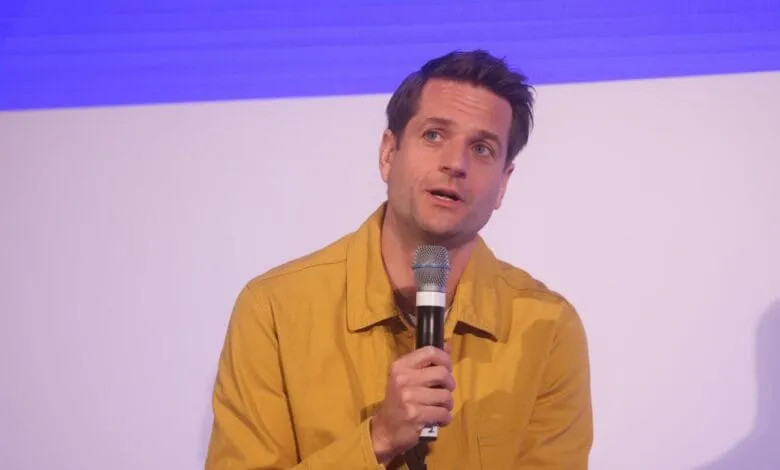 Klarna CEO in mustard yellow shirt speaks into microphone at a conference.