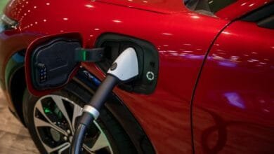 Close-up of a red electric car charging. A white charging cable is plugged into the car's charging port.